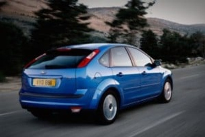Blue hatchback car driving on a countryside road with blurred trees and hills in the background, showcasing a used car in motion