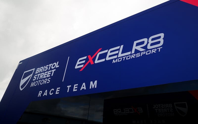 Signage on a blue building featuring logos and text for Bristol Street Motors and EXCELR8 Motorsport Race Team, emphasising association with used cars and new cars dealerships.