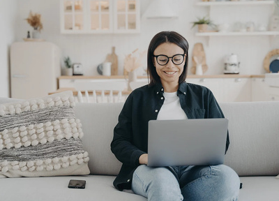 Female with glasses on sat on sofa with laptop
