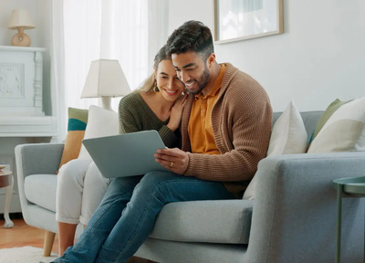female and male sat on sofa on laptop