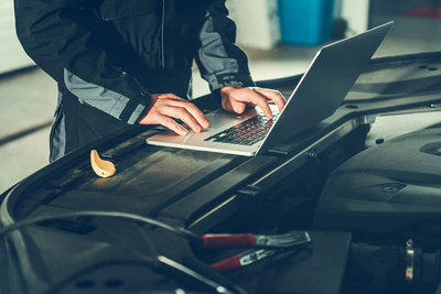 Mechanic working on laptop on a car engine