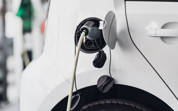 Close-up of a white electric car being charged with a cable plugged into the charging port near the rear wheel, illustrating modern vehicles among used cars and new cars.