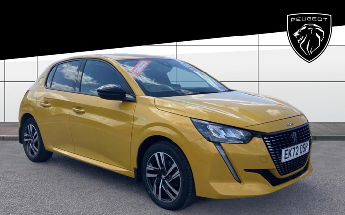 Yellow Peugeot 208 hatchback car with UK registration plate EK72 OSP parked in front of a Peugeot dealership wall with a large Peugeot lion logo. The car has a price sticker visible on the windscreen, indicating it is a used car available for sale, under the category of used cars and new cars.