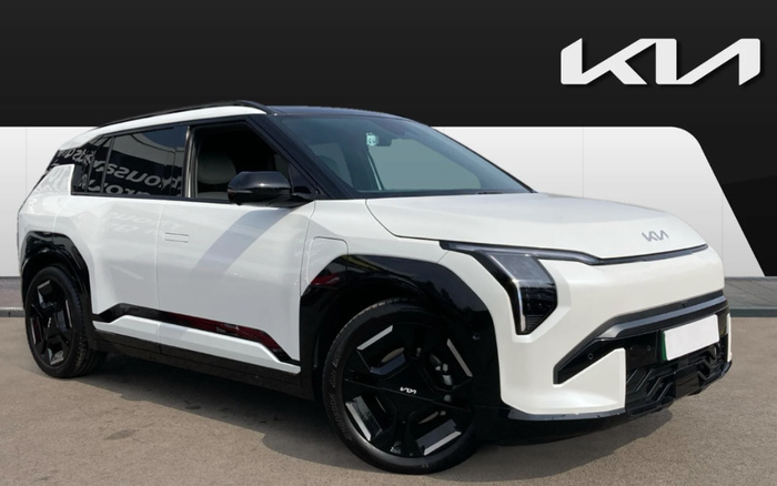 White and black Kia electric SUV parked in front of a modern black and white wall with the Kia logo displayed prominently in the top right corner, showcasing a sleek design ideal for used cars or new cars buyers seeking a contemporary vehicle.