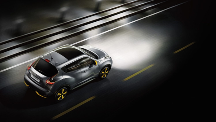 Overhead view of a grey Nissan Juke with yellow accents driving on a wet road at night, highlighting the car's sporty design and modern features, suitable for used cars or new cars buyers.