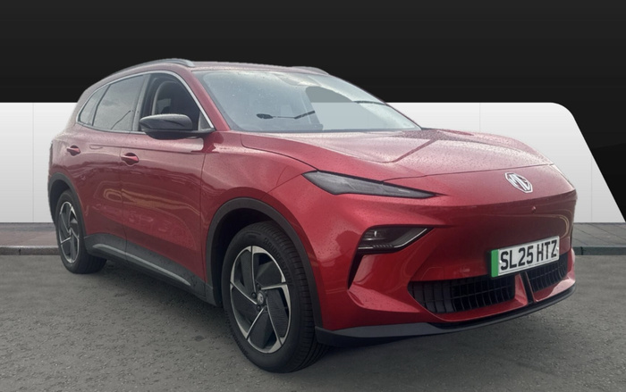 Red MG electric SUV with UK registration number SL25 HTZ parked on grey tarmac in front of a white and black background. The car is glossy with visible water droplets, modern front headlights, aerodynamic wheels, and black side mirrors. Suitable for buyers interested in used cars or new cars.