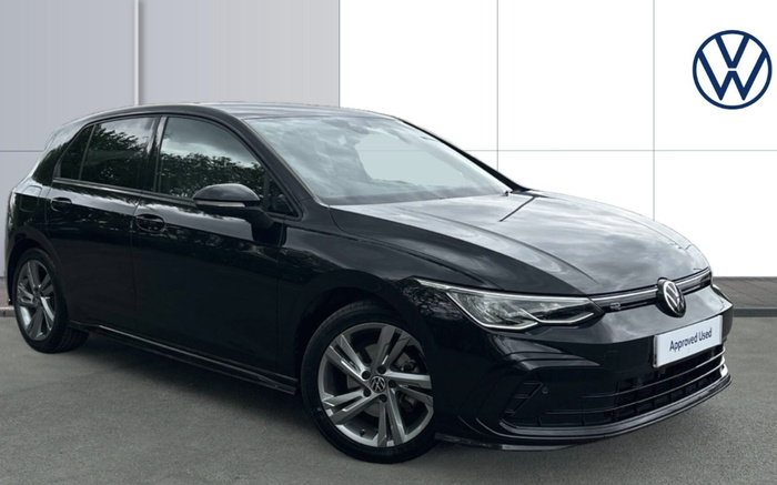 Black Volkswagen hatchback car parked on grey pavement with a white tiled wall background featuring the Volkswagen logo in blue on the upper right. The car has sleek modern headlights and sporty alloy wheels. The front license plate reads 'Approved Used,' indicating it is a certified pre-owned vehicle. The image highlights Volkswagen used cars and new cars options.