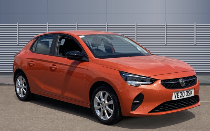 Orange Vauxhall hatchback car with registration plate VE20 OSK parked on pavement in front of grey corrugated metal wall. The car is in good condition, suitable for used cars or new cars listings.