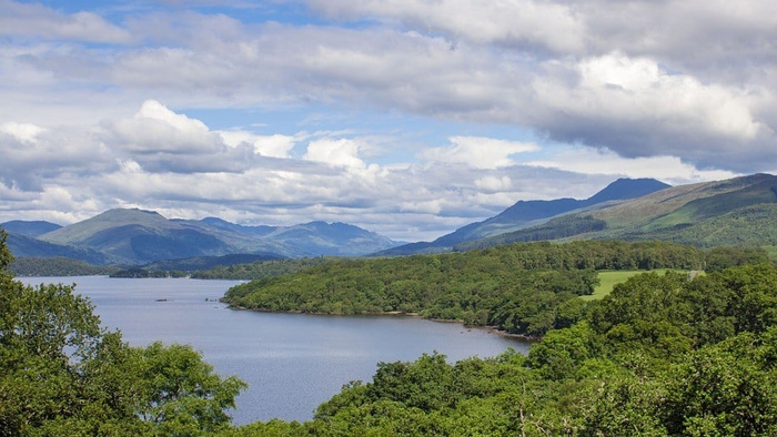 Scenic landscape featuring a large lake surrounded by dense green forests and rolling hills under a partly cloudy sky. No visible text or cars in the image to describe, focusing on natural scenery without references to used cars or new cars.