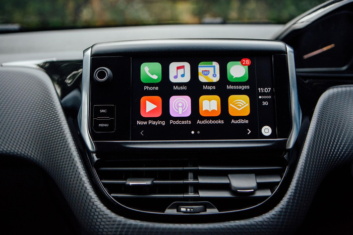 Car dashboard showing a touchscreen infotainment system with apps including Phone, Music, Maps, Messages with 28 unread, Now Playing, Podcasts, Audiobooks, and Audible. Time displayed is 11:07 with 3G signal visible. Surrounding dashboard features air vents and buttons marked SRC and MENU, highlighting technology features common in used cars and new cars.