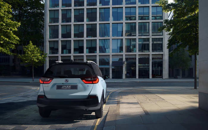Rear view of a light blue Honda Jazz Crosstar car parked on a city street near a modern glass office building, showcasing the vehicle's new design, highlighting available new cars and used cars options.