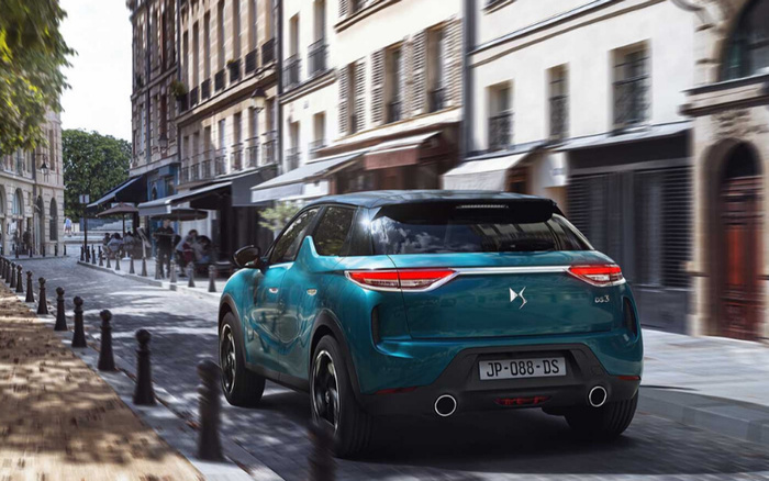 Teal DS 3 car driving down a cobbled city street with classic European buildings and outdoor cafes, license plate JP-088-DS, promoting both used cars and new cars in an urban setting.