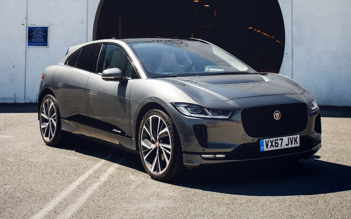 Grey Jaguar electric car parked in front of a large circular tunnel entrance on a sunny day, showcasing sleek modern design and alloy wheels, with a UK license plate VX67 JVK. Ideal for used cars and new cars buyers seeking luxury electric vehicles.