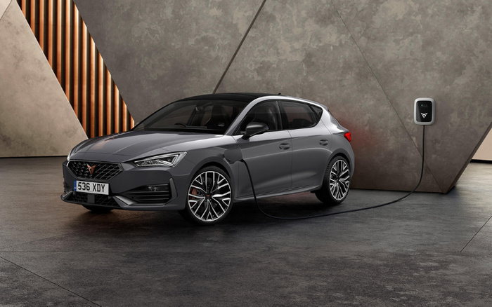 Grey electric hatchback car with UK license plate 536 XDY charging at a modern wall-mounted EV charger in an industrial-style indoor setting with textured concrete walls and geometric design elements, representing new cars and used cars.
