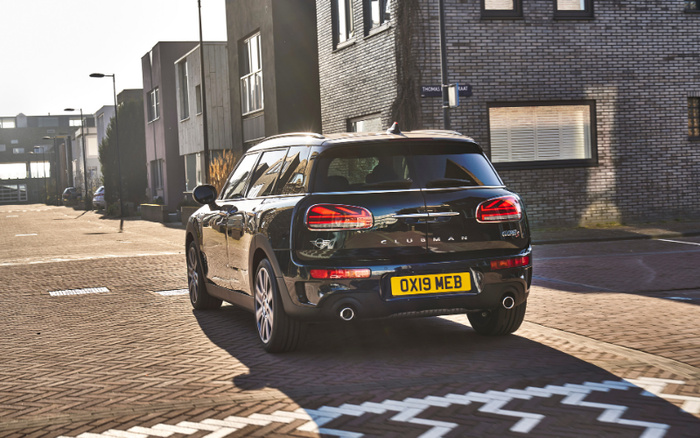 Black Mini Clubman Cooper S car with registration plate OX19 MEB driving on a sunny urban street with modern buildings around, showcasing a used car in excellent condition, suitable for buyers interested in used cars or new cars.