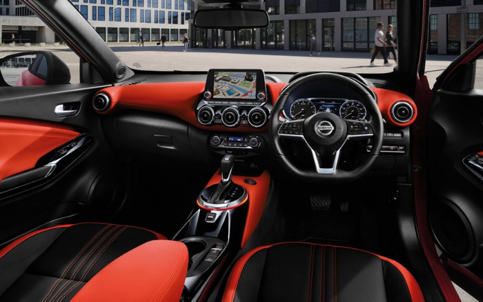 Interior view of a Nissan car showing the dashboard, steering wheel with Nissan logo, and centre console with gear shift. The seats and dashboard feature black and red leather upholstery with red stitching. The central touchscreen display shows a navigation map. The image highlights the modern, sporty design of this vehicle suitable for buyers interested in used cars or new cars.