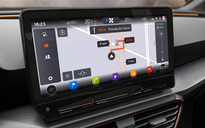 Close-up of a car dashboard touchscreen showing a detailed navigation map with route instructions to Passeig de Gràcia, including estimated times of 2, 6, and 7 minutes for different segments. The screen displays current time 16:23, temperature 20.5°C, and various control icons such as speed, phone, and music. The dashboard has sleek black and silver finishes, and the image highlights modern car technology suitable for both used cars and new cars.