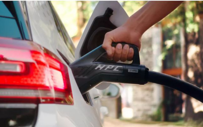 Close-up of a white car being charged with an HPC electric vehicle charger, showing a hand holding the charger plugged into the vehicle's charging port, emphasising electric vehicles as part of the selection of used cars and new cars.