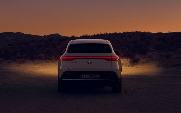 Rear view of a white Mercedes-Benz EQB 400 4MATIC electric SUV with license plate S N 2932 E, parked on a desert road at sunset with hills in the background, showcasing a modern design used for advertising new cars and used cars.