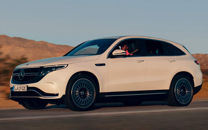 White Mercedes-Benz EQC electric SUV driving on a road with desert mountains in the background, featuring modern black alloy wheels and distinctive front grille with the Mercedes logo, highlighting options for used cars and new cars.
