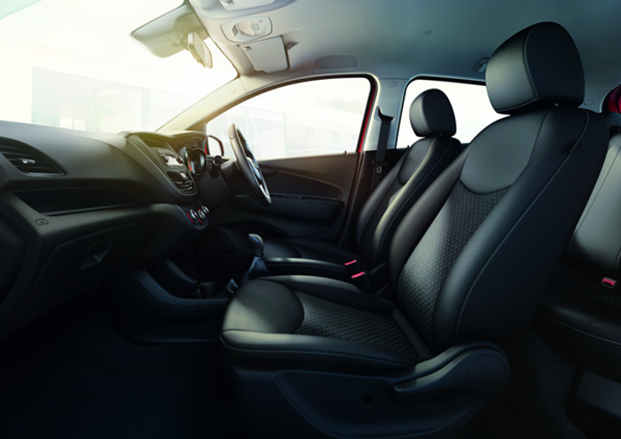 Interior view of a modern car showing front seats, dashboard, steering wheel, gear stick, and controls. The car features dark fabric seats with patterned upholstery, a clean and sleek dashboard design with air vents and control knobs, and a sunroof overhead. This image is suitable for advertising used cars and new cars.