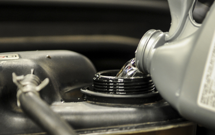 Close-up of engine oil being poured from a grey container into the oil filler cap of a car engine, highlighting car maintenance essential for both used cars and new cars.
