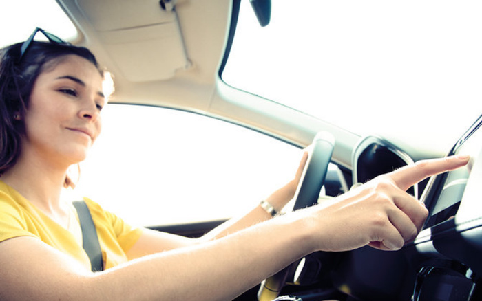 Woman in a yellow top sitting in the driver's seat of a car, smiling and using the touchscreen interface on the dashboard, representing the modern technology found in used cars and new cars.