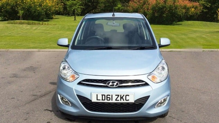 Front view of a light blue Hyundai car parked on a driveway with a green lawn and bushes in the background. The car registration plate reads LD61 ZKC. This image is suitable for advertising used cars and new cars.