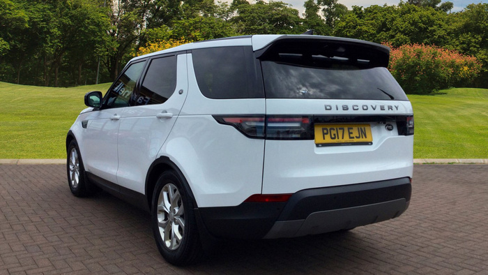 White Land Rover Discovery SUV parked on a brick driveway with green grass and trees in the background, showing rear and side view, UK registration plate PG17 EJN, with dark tinted rear windows and silver alloy wheels, suitable for used cars or new cars options.