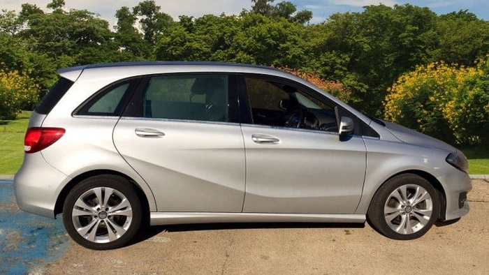 Silver compact hatchback car parked on a driveway with lush green trees and bushes in the background, representing a typical used car or new car available for sale.