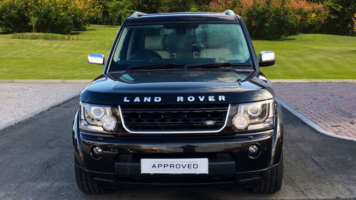 Front view of a black Land Rover with 'LAND ROVER' text on the hood and an 'APPROVED' licence plate, parked on a driveway with green grass and trees in the background, ideal for showcasing used cars or new cars.