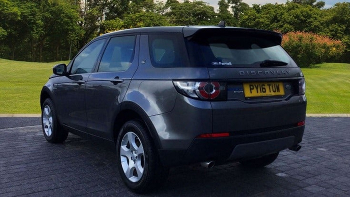 Dark grey Land Rover Discovery Sport parked on a paved driveway with green grass and trees in the background, showing rear and side view, featuring UK registration plate PY16 TUW, suitable for used cars and new cars listings.