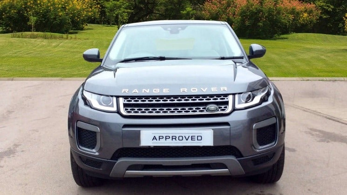 Front view of a grey Range Rover vehicle parked on a driveway with green bushes and grass in the background. The car has a grille with the Land Rover badge and the word 'RANGE ROVER' visible on the front. The license plate reads 'APPROVED', indicating it is a certified used car. This image is relevant for advertising used cars and new cars, showcasing a high-quality, approved pre-owned Range Rover.