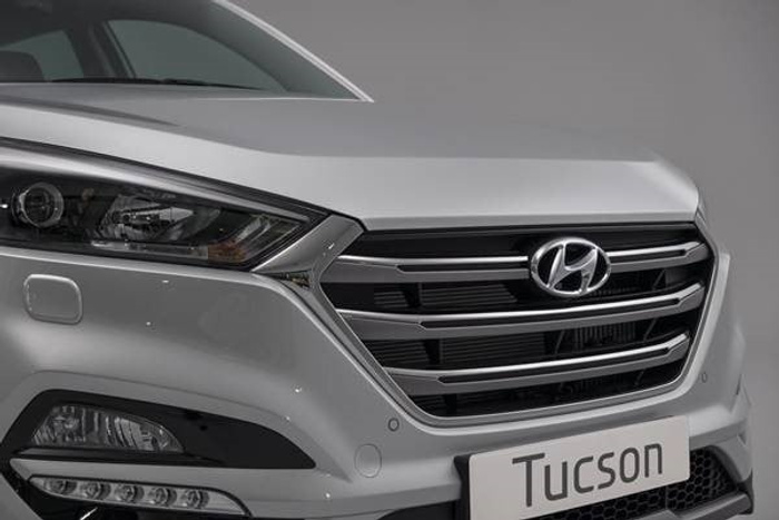 Close-up image of the front grille and headlight of a silver Hyundai Tucson car, showcasing the Hyundai logo and the Tucson nameplate, representing used cars and new cars.