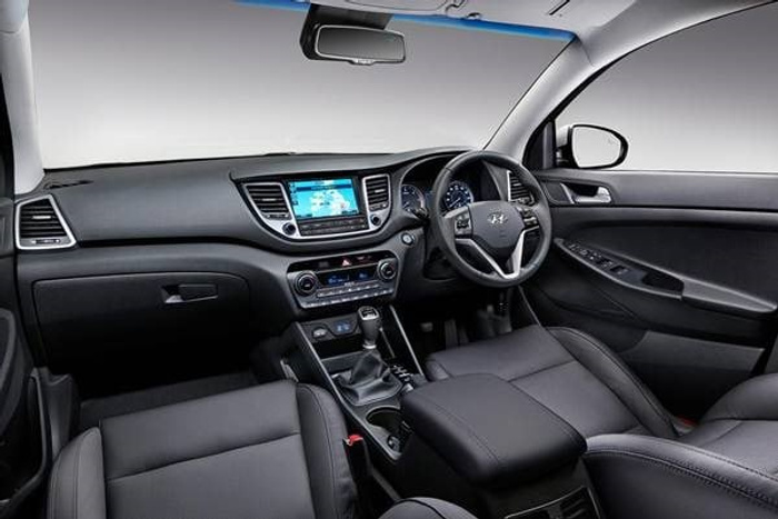 Interior view of a modern Hyundai car featuring a black dashboard, multi-function steering wheel, touchscreen infotainment system, manual gear stick, and leather seats, showcasing a clean and spacious design ideal for used cars and new cars buyers.