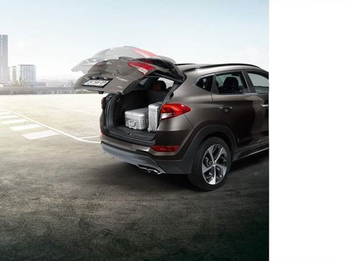 Dark brown SUV with open rear tailgate showing spacious boot containing a silver suitcase, parked on a concrete rooftop with city buildings in the background, illustrating a practical and modern vehicle ideal for both used cars and new cars buyers.