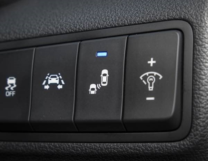 Close-up image of car dashboard control buttons including traction control off, lane keeping assist, blind spot monitoring with a blue indicator light, and dashboard illumination brightness adjustment with plus and minus symbols, highlighting features common in used cars and new cars.