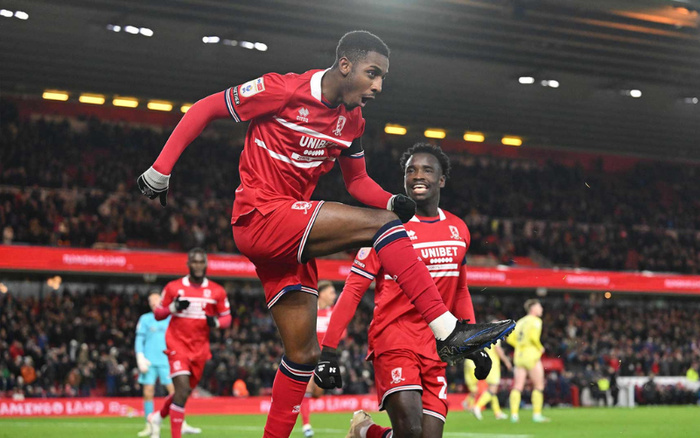 Football players in red Middlesbrough FC kits celebrating on the pitch during a match in a large stadium with a final score board showing Middlesbrough 1 vs Sunderland 0. The main player is mid-air with a clenched fist, while another player is smiling beside him. The crowd is visible in the background under stadium lights. This image does not depict used cars or new cars.