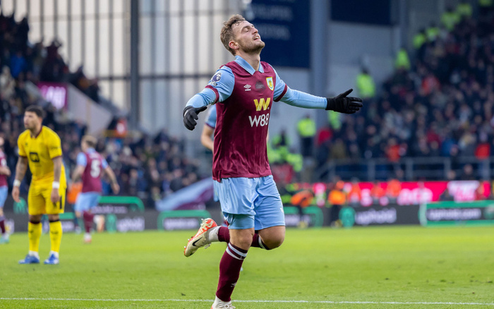 Burnley football player in claret and blue kit with W88 sponsor logo on the chest, walking on the pitch with arms outstretched and eyes closed during a match, surrounded by players and crowd in the background. No visible text about used cars or new cars.