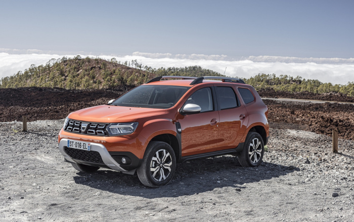 Orange Dacia Duster SUV parked on a gravel road with a mountainous background under a cloudy sky, showcasing the vehicle's robust design and alloy wheels, suitable for both used cars and new cars buyers looking for a reliable and stylish compact SUV.