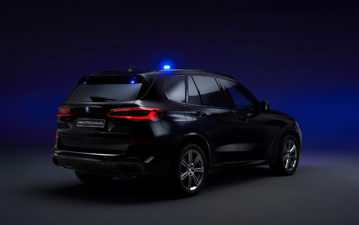 Rear and side view of a black BMW X5 SUV with illuminated blue lights on top, shown against a dark blue and black gradient background. The license plate reads 'BMW X5 PROTECTIVE V8S'. This image highlights the sleek design of a new car, ideal for use in advertising used cars and new cars.