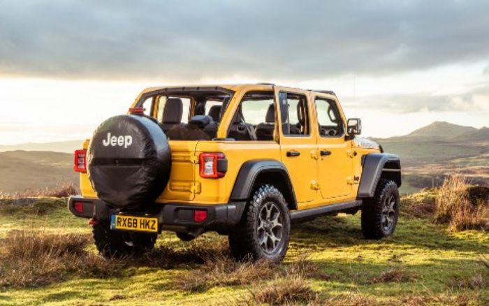 Yellow Jeep Wrangler with black removable roof and spare tire cover displaying 'Jeep' parked on grassy terrain with hills in the background, registration plate RX68 HKZ, showcasing rugged new cars and used cars in an outdoor setting.