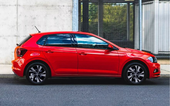 Side view of a shiny red hatchback car parked on a street in front of a modern building with large windows, suitable for used cars and new cars advertisements.