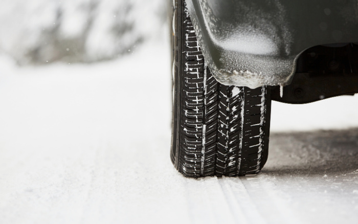 Close-up of a car tyre driving on a snowy road with snow and ice on the tyre tread and mudguard, illustrating winter driving conditions for used cars and new cars in cold weather.