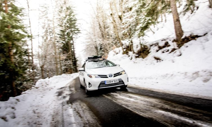 White Toyota car with roof rack driving on a snow-covered road flanked by snowy trees, UK registration plate GU64 SUU, illustrating used cars and new cars in winter conditions