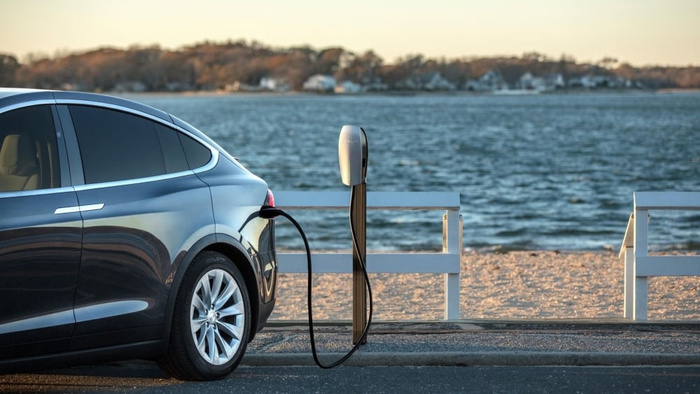 Black Tesla electric car charging at a Tesla charging station by the seaside with water and distant trees in the background, illustrating modern new cars and the growing trend of electric used cars.