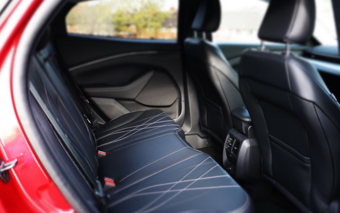 Interior view of the backseat of a red car featuring black leather seats with white stitching, modern door panel design, and rear air vents. The image highlights the spacious and clean rear passenger area, suitable for showcasing used cars or new cars.