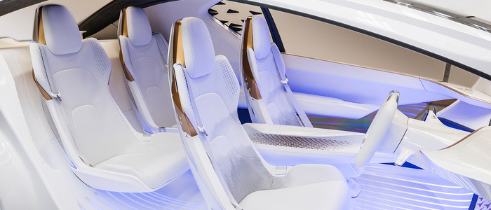 Interior view of a futuristic car showing four white ergonomic seats with brown accents and integrated seat belts, a white steering wheel, and a sleek dashboard, illuminated by soft blue ambient lighting, representing modern design often seen in new cars and used cars sales promotions.