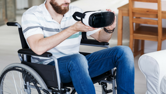 Man in a wheelchair holding a virtual reality headset in a modern living room, illustrating adaptive technology and accessibility; image relevant for promoting used cars and new cars with inclusive features.