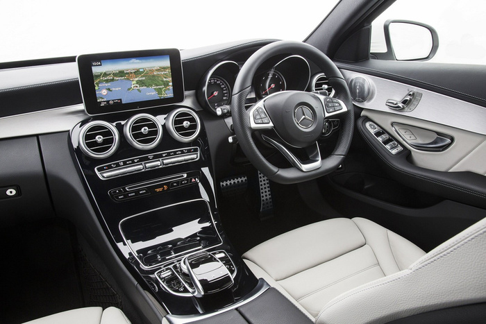 Interior of a modern Mercedes-Benz car featuring a digital navigation screen showing a map of the UK, black and silver dashboard with three circular air vents, multifunction steering wheel with Mercedes logo, beige leather seats, and controls on the driver's door. Perfect example of luxury used cars and new cars with advanced technology and stylish design.